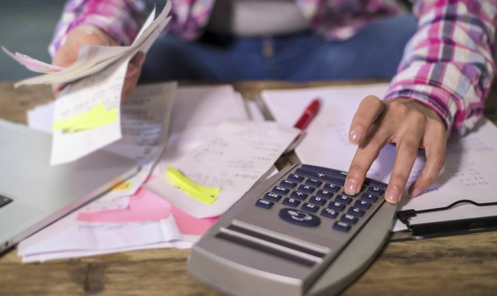 Women's hand with calculator, surrounding by receipts and other financial papers.