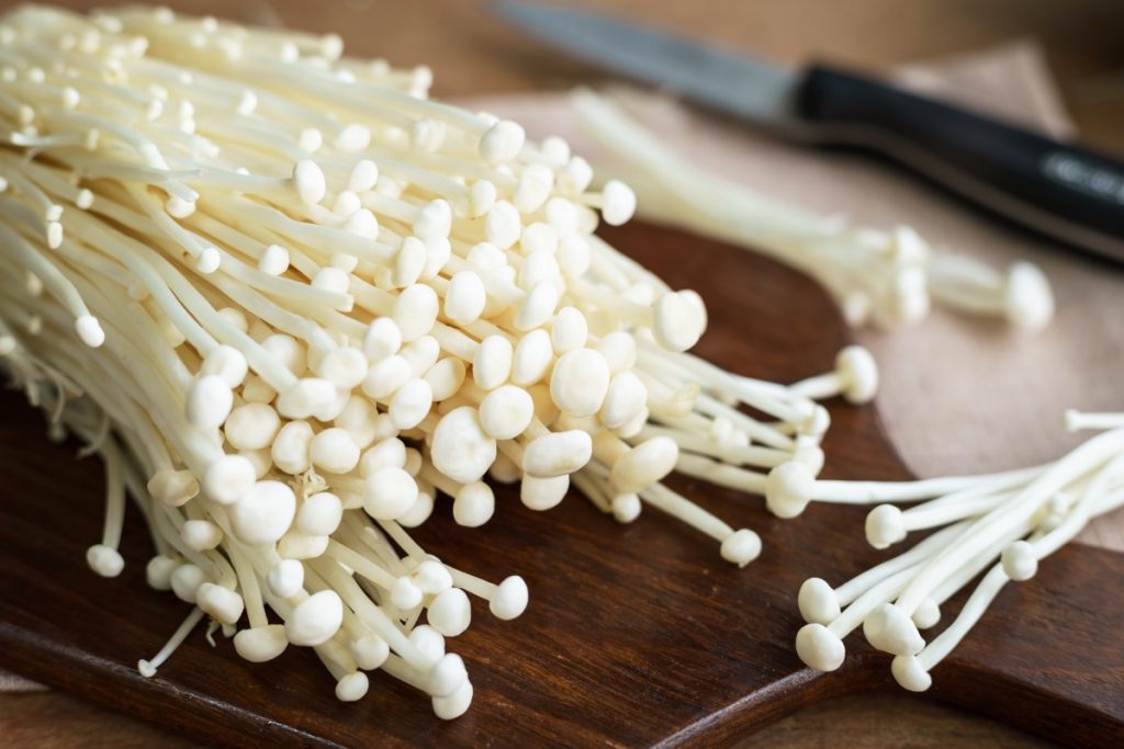 Cultivated enoki mushrooms on a wooden chopping board