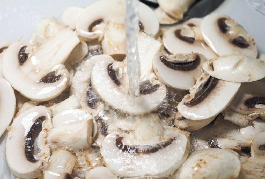 Sliced mushrooms being rinsed under running water.