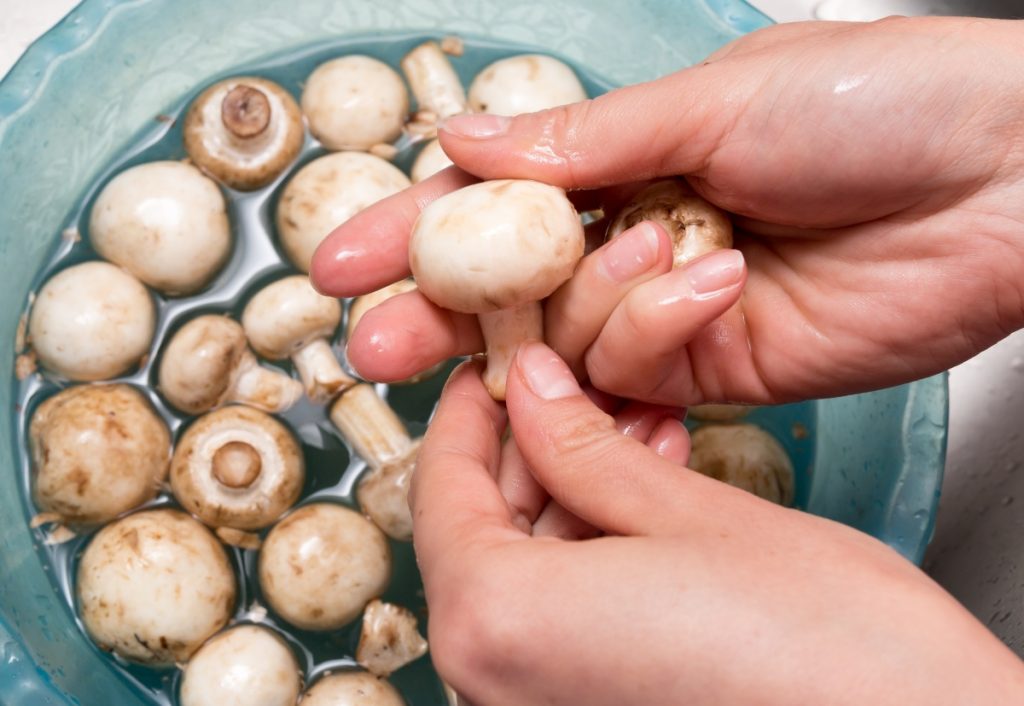 Washing button mushrooms in a bowl of water.