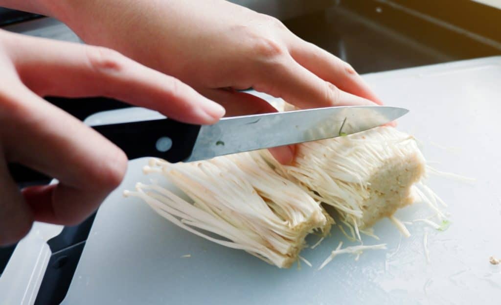 Trimming off the base of a cluster of enoki mushrooms